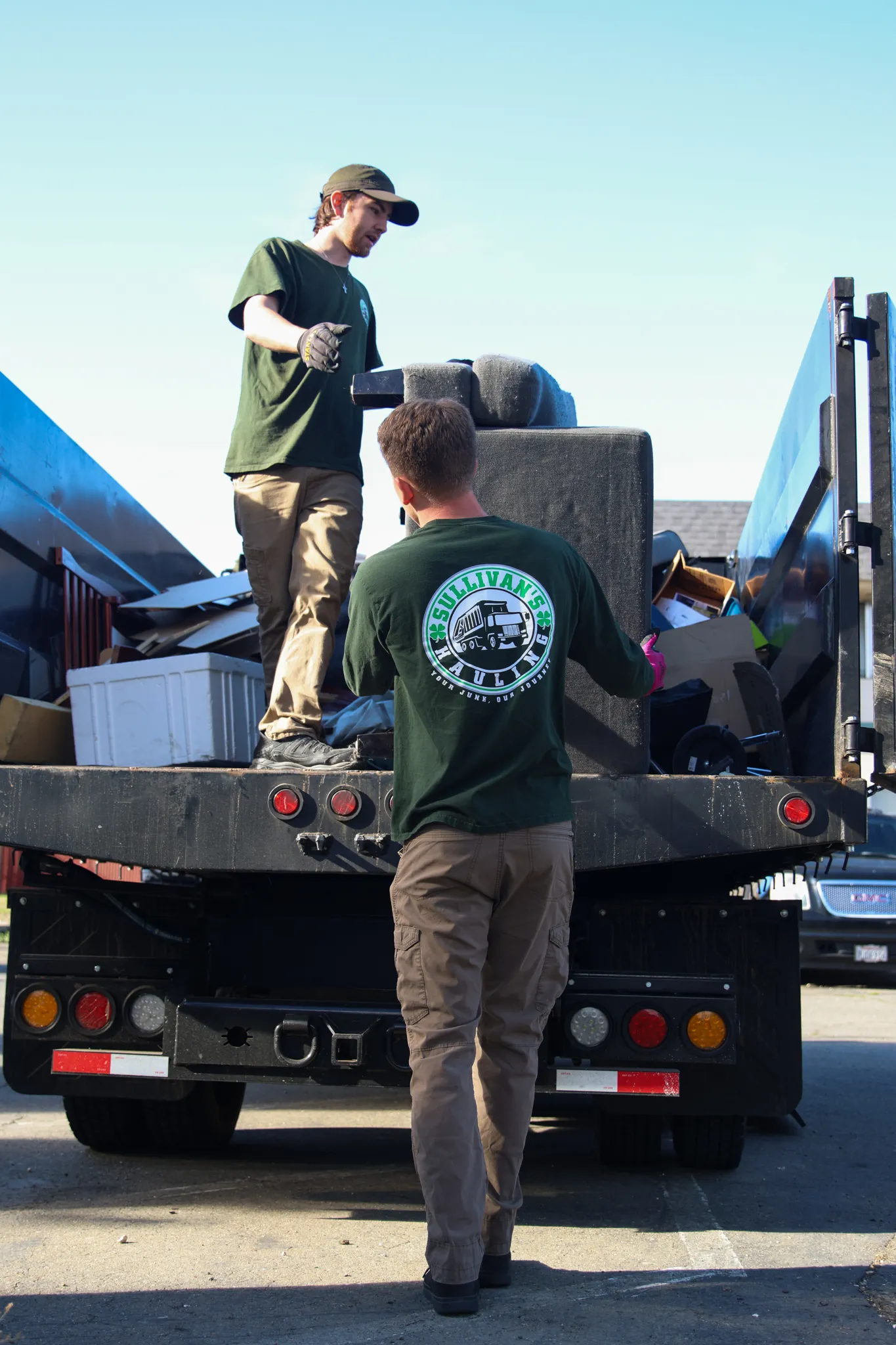 Two Sullivan's Hauling crew members lifting a couch cushion onto the back of the truck