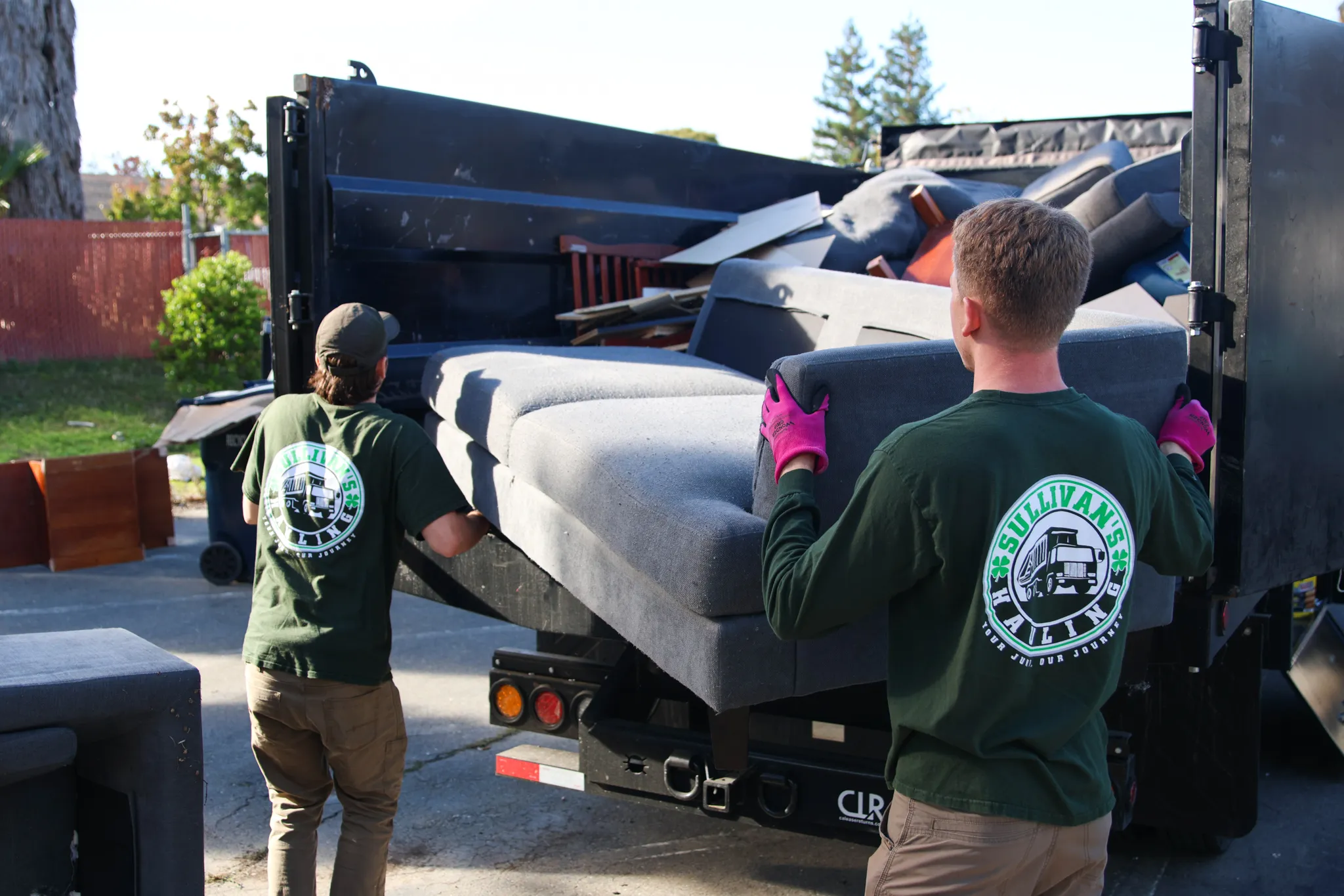 Two Sullivan's Hauling crew members lifting a gray sectional sofa into the truck bed